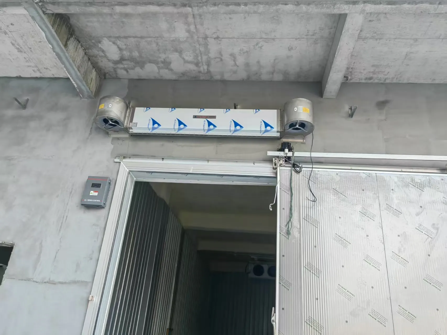 Centrifugal cold storage air curtain installed above a cold room door to reduce cold air loss and prevent warm air infiltration.